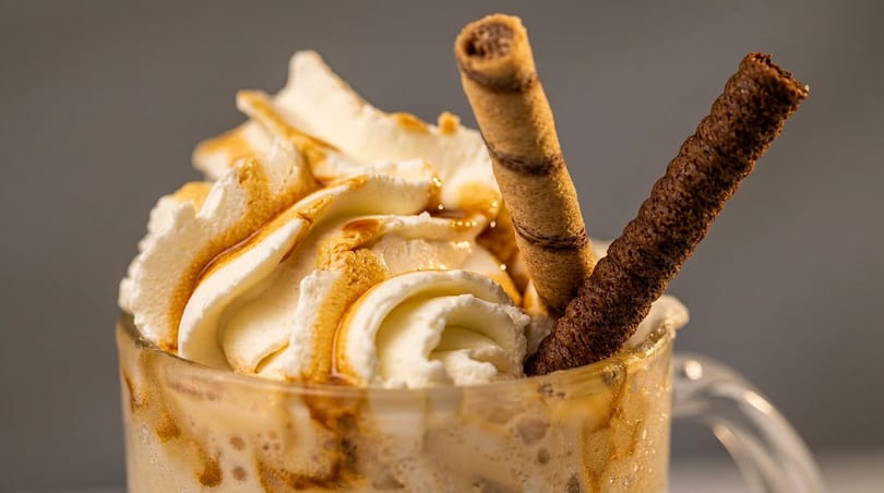 Creamy drink with caramel drizzle, whipped cream, and two wafer sticks.